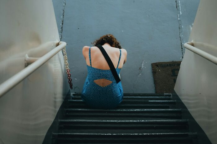 Woman in a blue dress sitting on stairs with her head down, reflecting worries women face daily in life.
