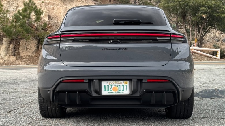 A rear shot of the Slate Grey Neo Macan GTS Electric parked on asphalt in front of trees and a mountain face