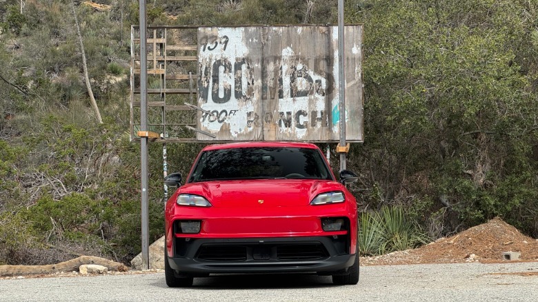Head-on shot of a Carmine Red Macan GTS Electric parked in front of the dilapidated Newcombs Ranch sign and trees