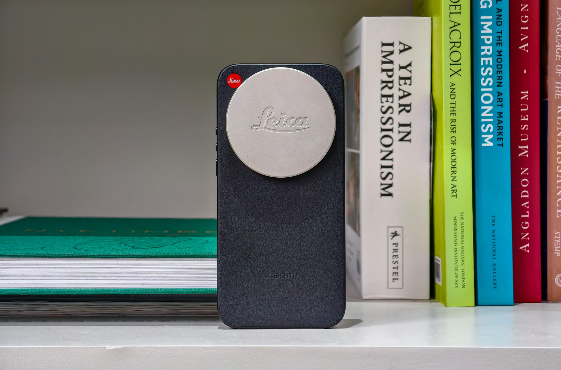 Photo of the Xiaomi Leica Leitzphone on a bookshelf, in a case with a Leica lens cap