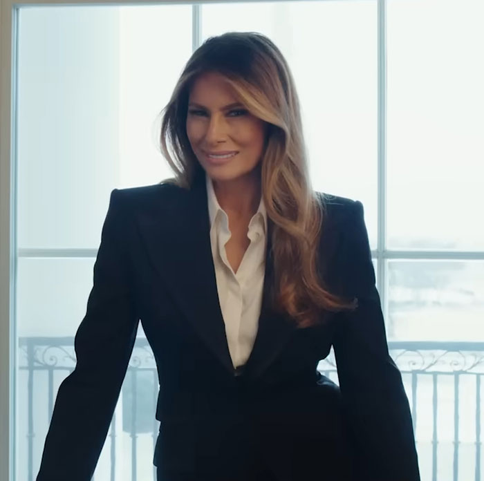 Woman in black blazer and white shirt smiling confidently in front of window, related to theater's hilarious clap back and Amazon pull.