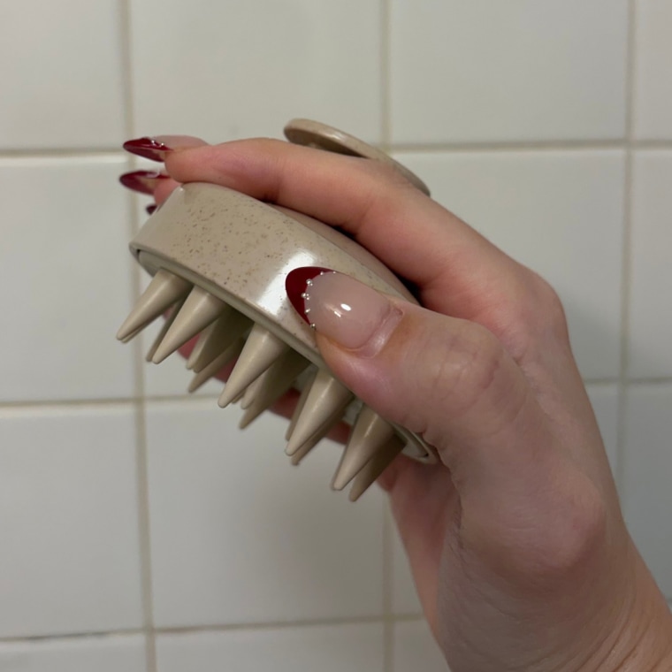 Woman holding a scalp massager against tile wall