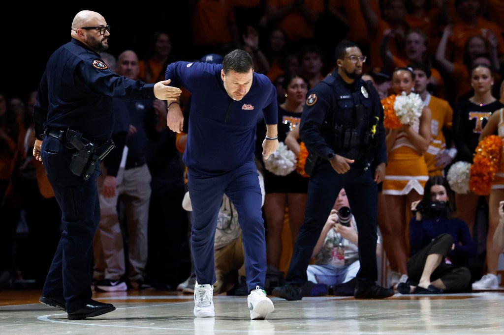An officer restraining Mississippi head coach Chris Beard after he was ejected from a basketball game.