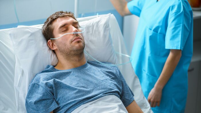Young man in hospital bed with nasal oxygen tube, representing people who’ve been in a coma and PTSD experiences.