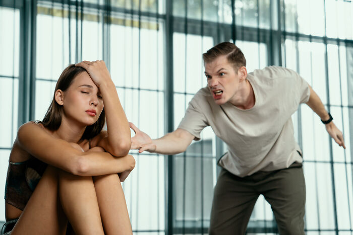 A distressed woman sitting with head in hand as a man angrily yells, illustrating PTSD and trauma after coma experiences.