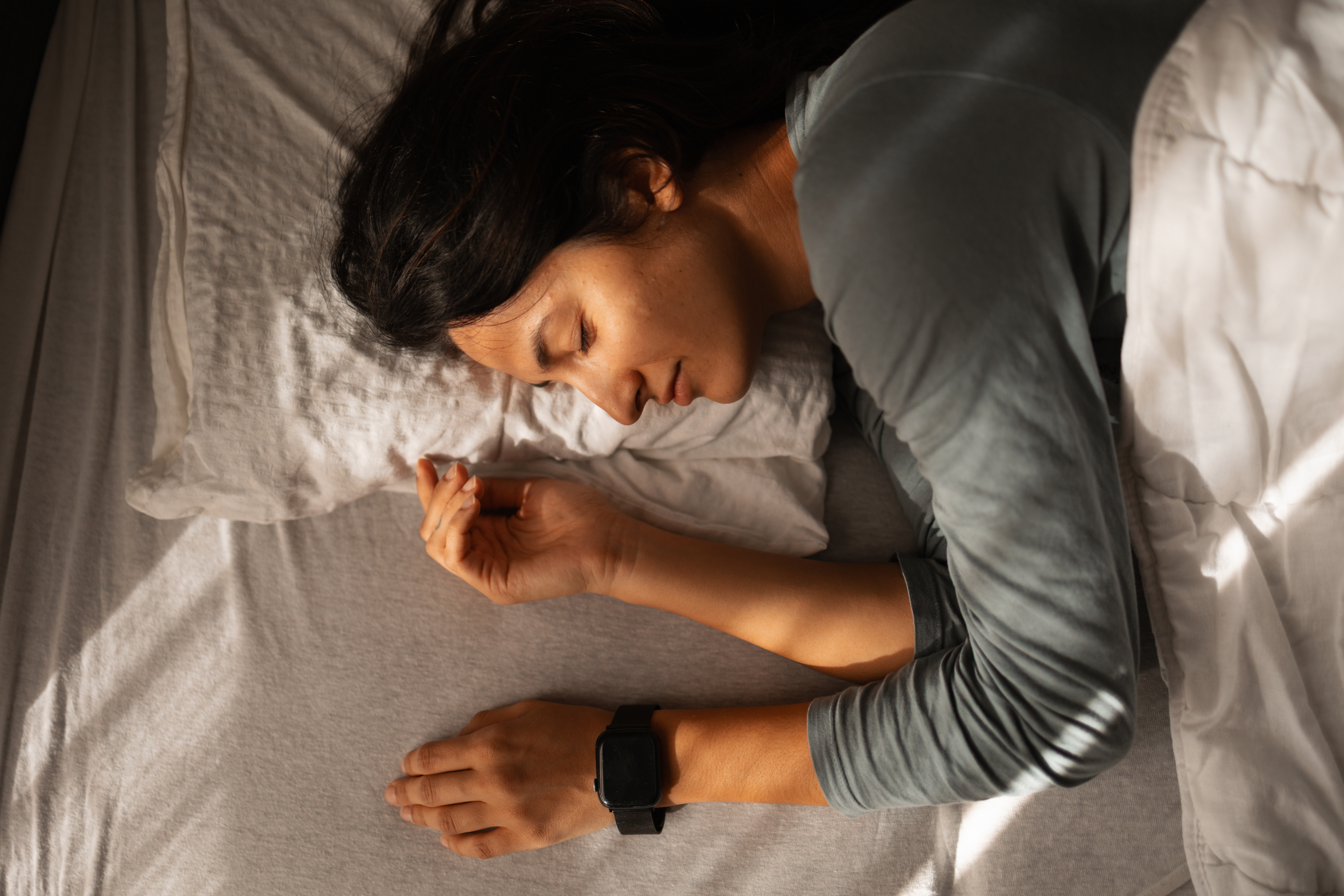 A woman lies asleep on her front in bed with a wrist-worn sleep tracker on her left wrist.