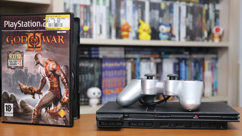 A PS2 Slim with a silver controller, and a God of War 2 game case