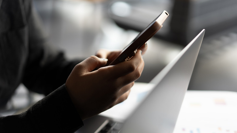 Someone holding their cellphone over a computer
