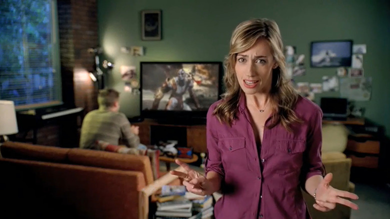 A mom standing in front of her son as he plays God of War on TV in a PlayStation 3 commercial.