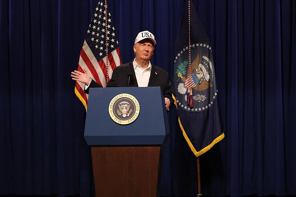 A person in a "USA" cap speaks at a podium with a presidential seal and flags in the background