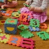 Children play with colorful, numbered puzzle pieces on the floor. Their faces are not visible.