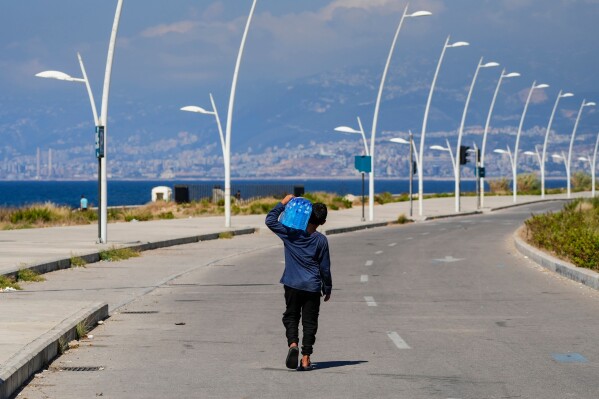 A young street vendor carries a pack of water bottles as he looking for customers during a sweltering day on the Mediterranean Sea corniche in Beirut, Lebanon, July 20, 2023. (AP Photo/Hassan Ammar, File)