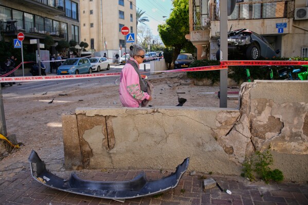A woman walks past a cordoned-off area damaged during an Iranian strike in Tel Aviv, Israel, Sunday, March 8, 2026. (AP Photo/Ohad Zwigenberg)