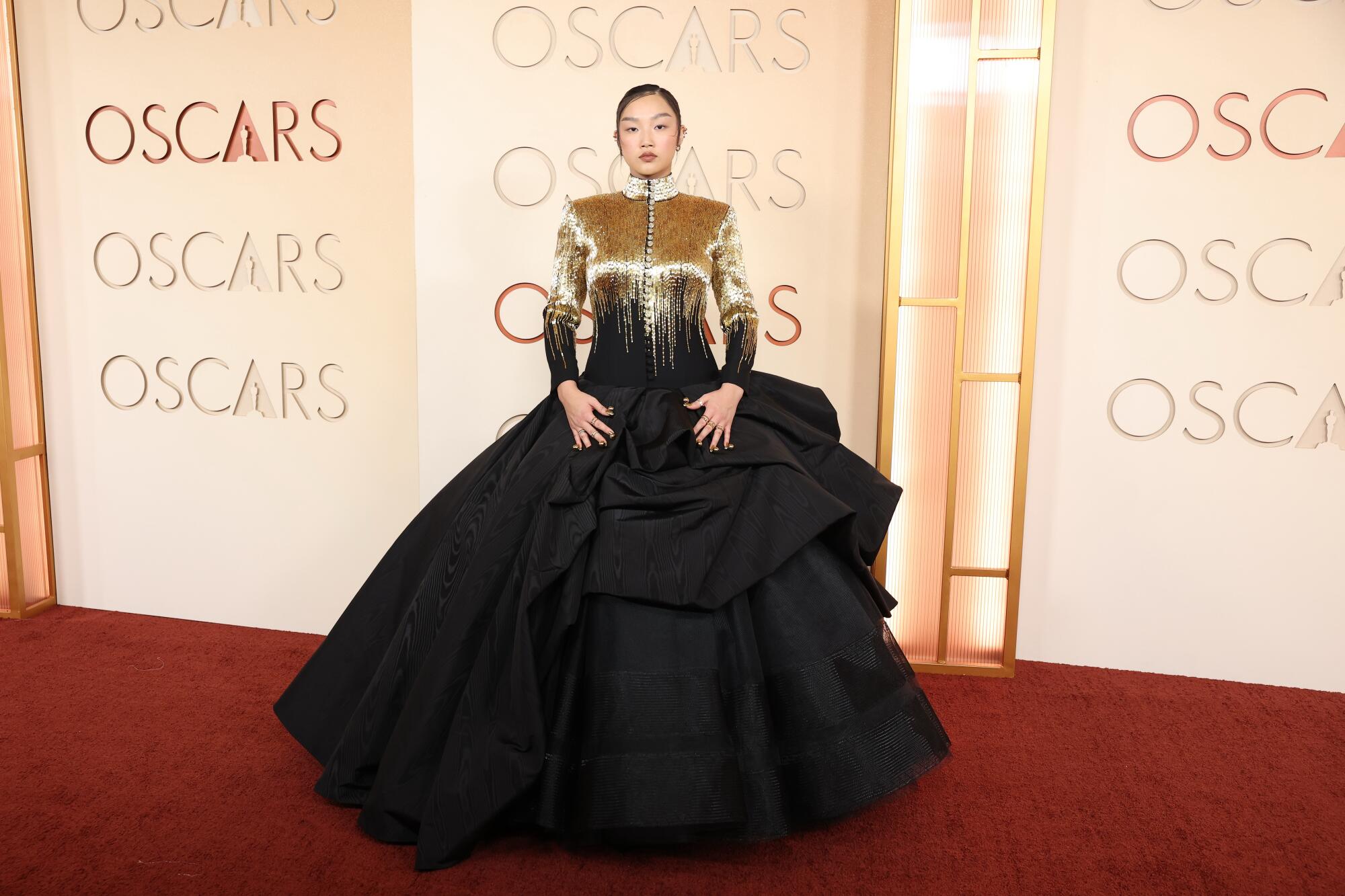 Audrey Nuna, wearing a black ballgown with gold top, poses on the red carpet. 