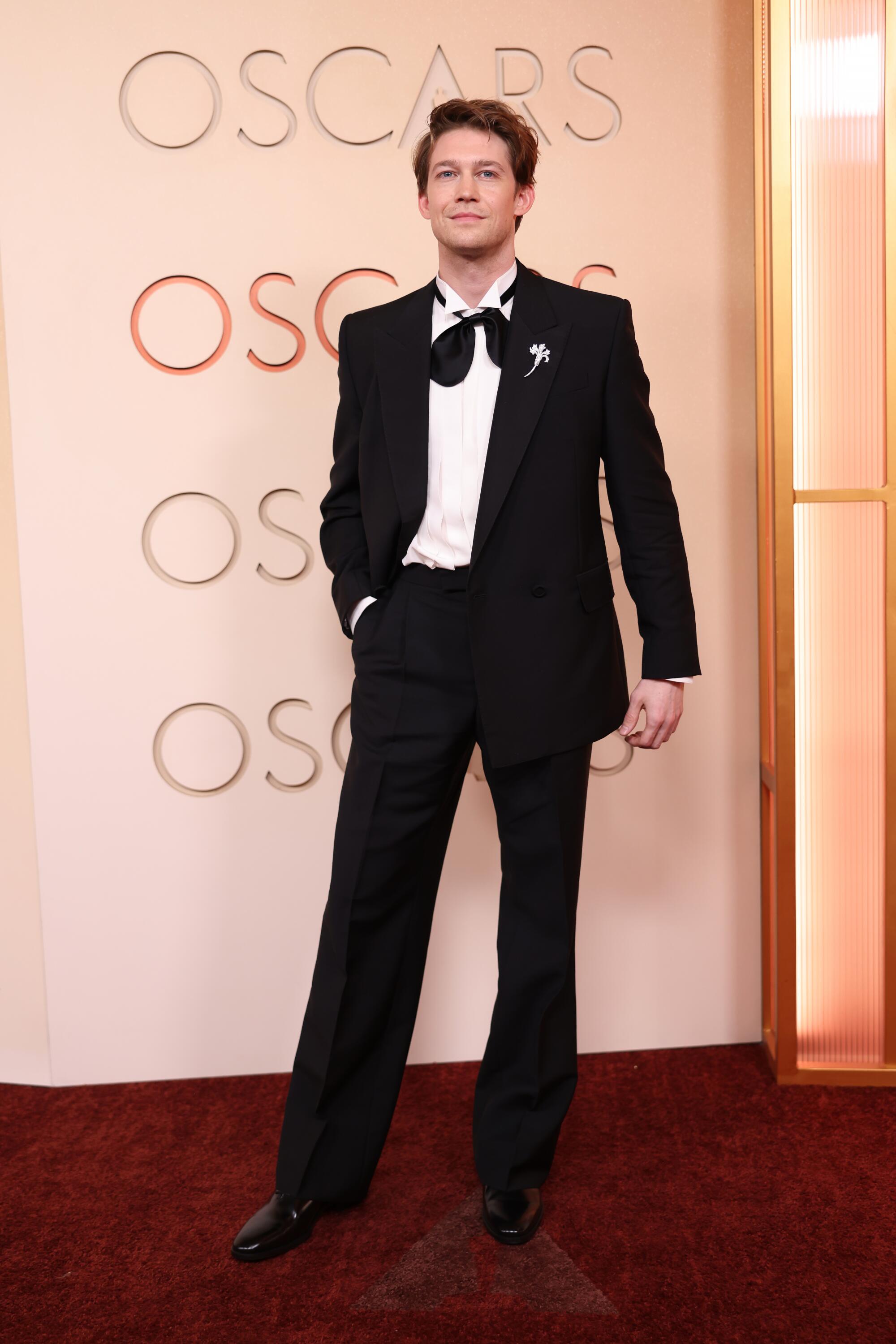 Joe Alwyn, in a black tux, poses on the red carpet. 