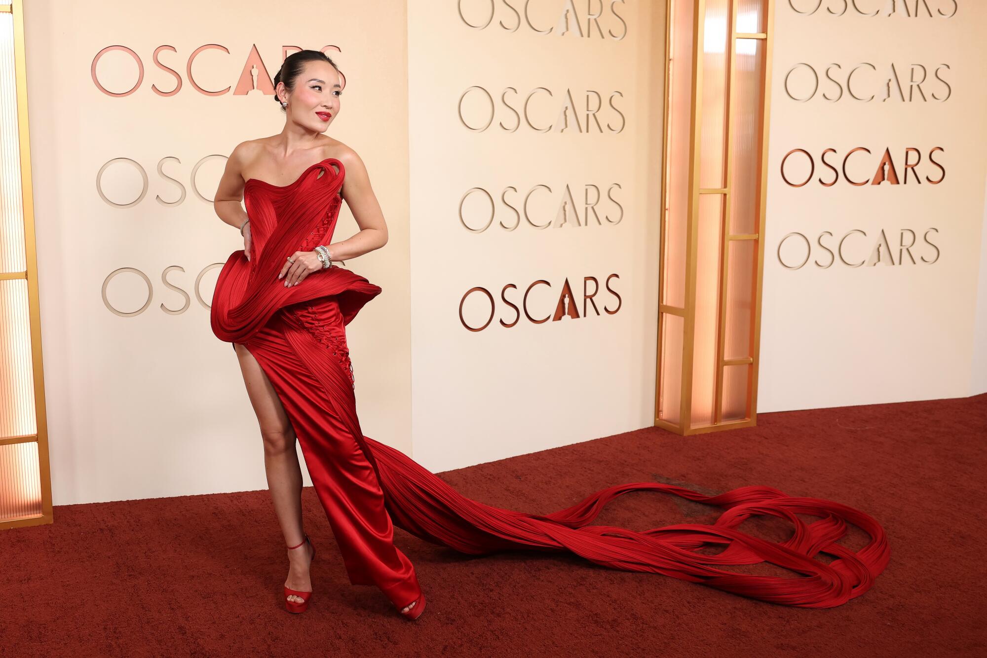 Li Jun Li, wearing a red gown with a high slit and a long train, poses on the red carpet. 