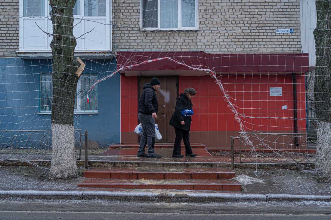 Civilians walk along Izium's city streets where nets overhang.
