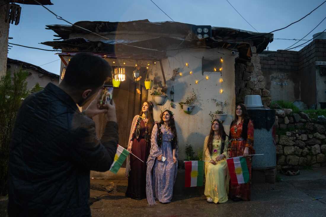 Women pose for photos dressed in traditional Kurdish clothing, which are colorful, long dresses and floral necklaces and head pieces.
