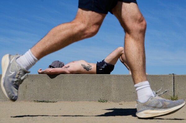 A jogger runs past as a man sunbathes at Crissy Field in San Francisco, Tuesday, March 17, 2026. (AP Photo/Godofredo A. Vásquez)
