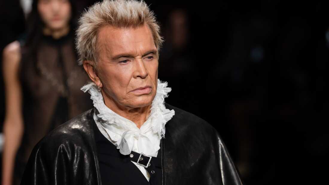 Billy Idol walks the runway during the Ann Demeulemeester Womenswear Fall/Winter 2026-2027 show as part of Paris Fashion Week in Paris, France. He is wearing a black leather coat and a white, ruffled, collared top underneath. 