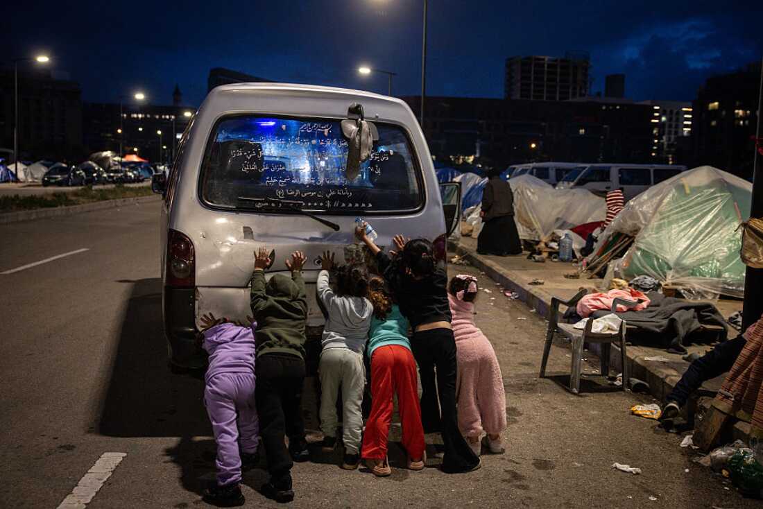 Displaced children help to push start the families van at a temporary displacement camp near the Lebanon port on March 27, 2026 in Beirut, Lebanon.