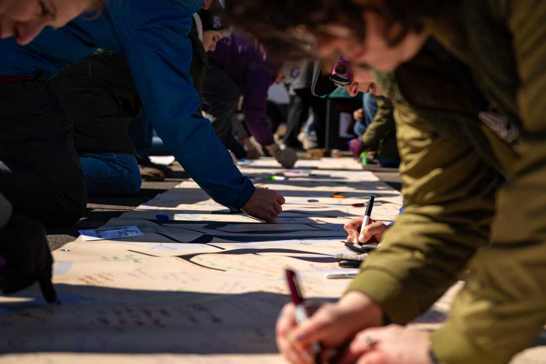 HARTFORD, CONNECTICUT, MARCH 28, 2026: Thousands sign a banner that says “We the People” at the “No Kings” protest at the capitol in Hartford on March 28, 2026. (Tyler Russell/Connecticut Public)