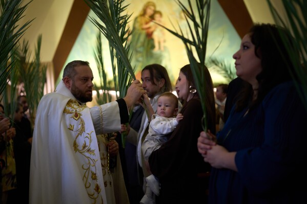 A priest blesses the palm branches held by the worshippers during a Palm Sunday Mass at the Our Lady of Hadat Church in Beirut, Lebanon, Sunday, March 29, 2026. (AP Photo/Emilio Morenatti)