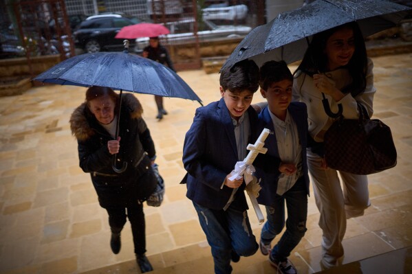 Worshippers shelter from the rain under umbrellas as they arrive at a church to attend a Palm Sunday Mass in Beirut, Lebanon, Sunday, March 29, 2026. (AP Photo/Emilio Morenatti)