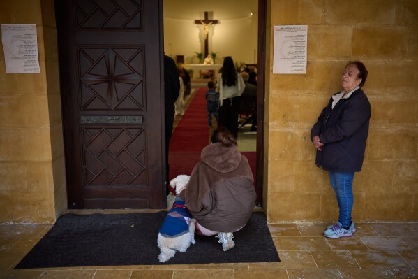 A Catholic woman kneels beside her dog at the entrance of a church during a Palm Sunday Mass in Beirut, Lebanon, Sunday, March 29, 2026. (AP Photo/Emilio Morenatti)