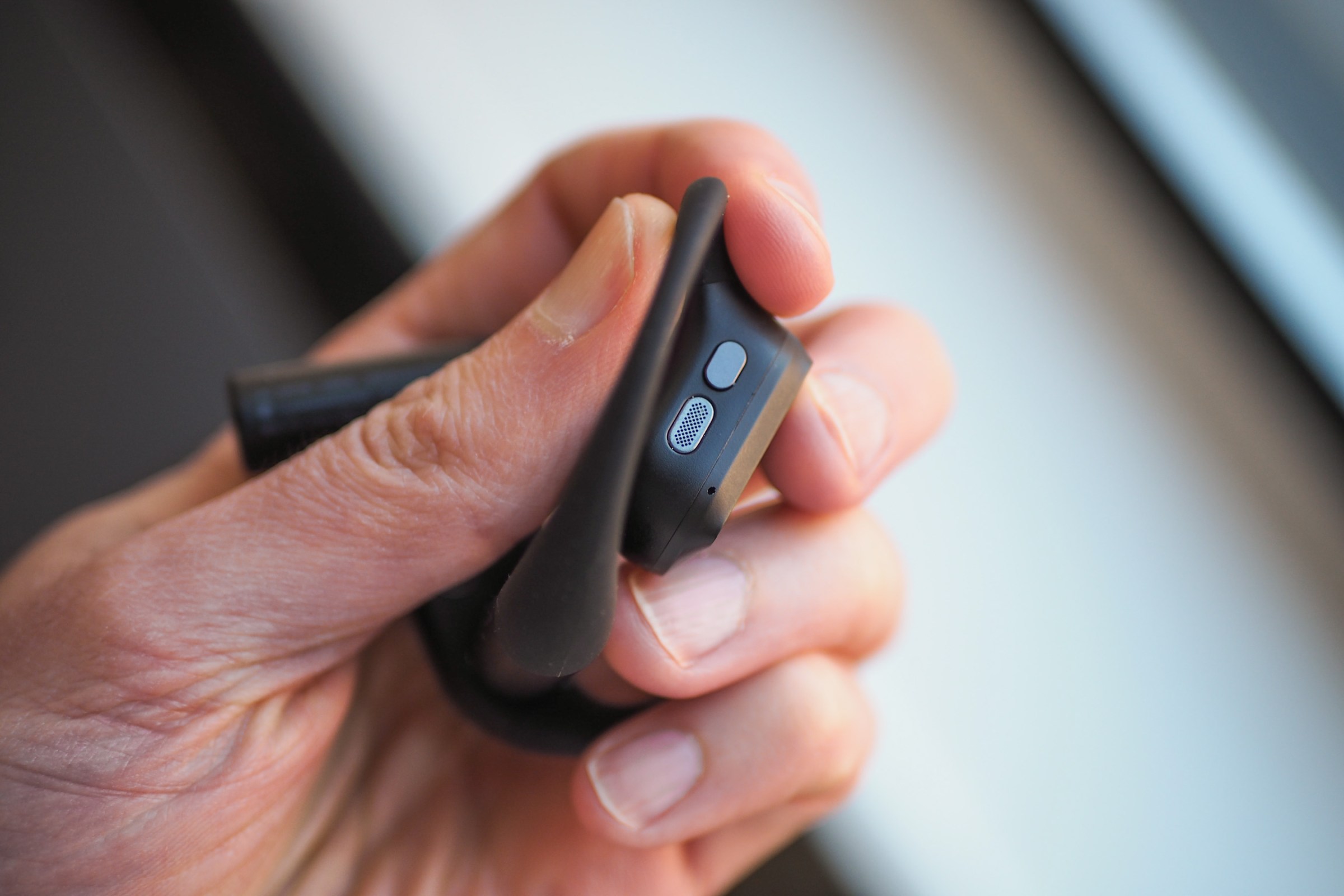 An image that shows a person holding one of the Asus Cetra Open Wireless earbuds in a way to show its top-mounted button.
