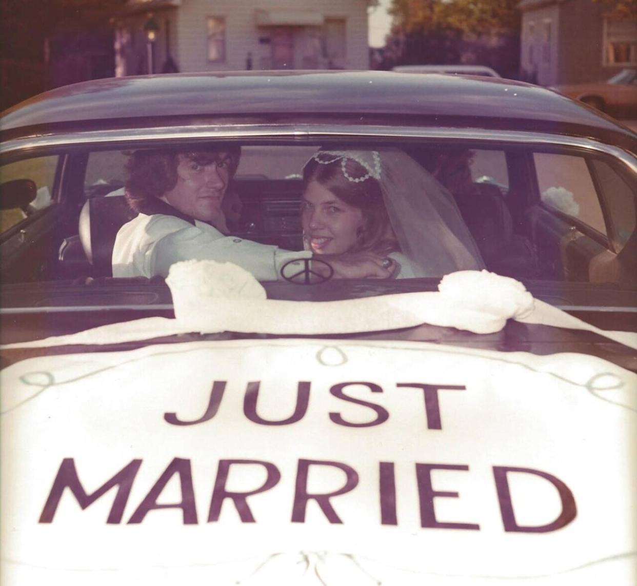 A couple inside a car looking through the back window at the camera. Just Married is painted on the trunk. -