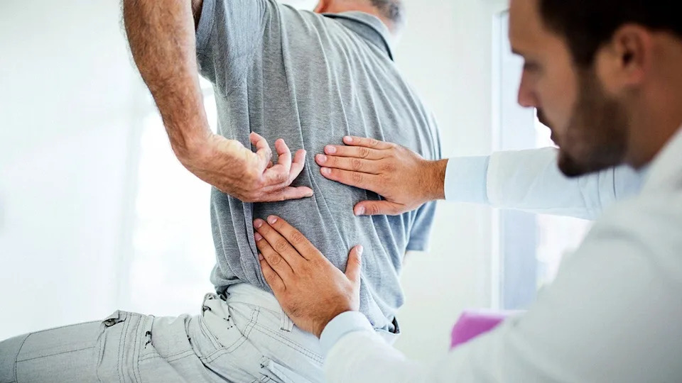 Senior man pointing to his lower back while sitting in a doctor's office with a male doctor.