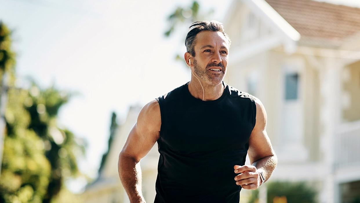 Runner, fitness and senior man running, listening to music outdoor in neighborhood for workout wellness, energy and healthy lifestyle motivation. Sports person with exercise training goal in street