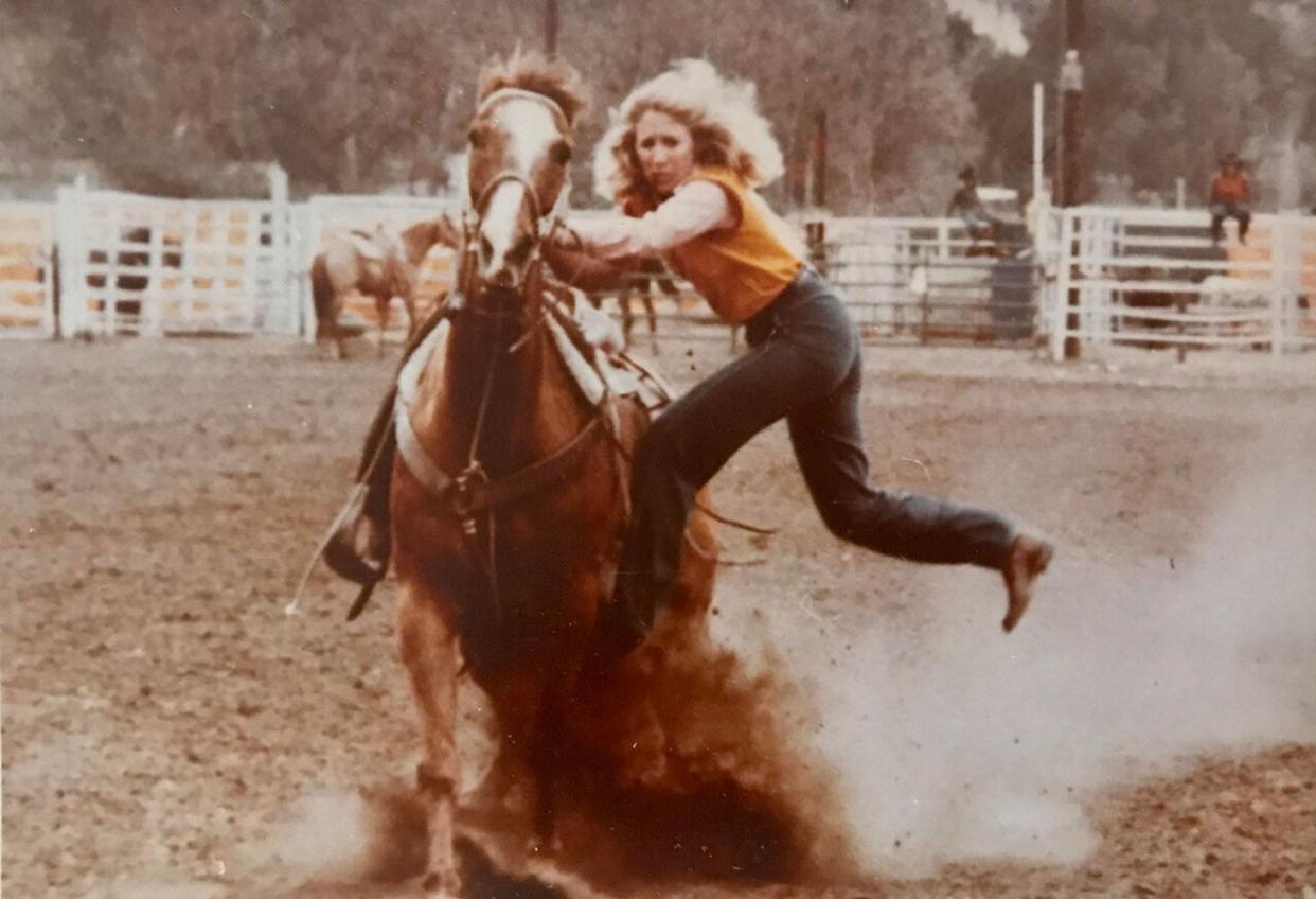 A woman riding a horse in a rodeo, kicking up dust -