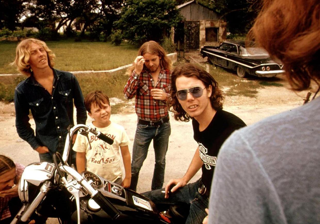 A man on the back on a motorcycle on the side of a road talking with some friends -