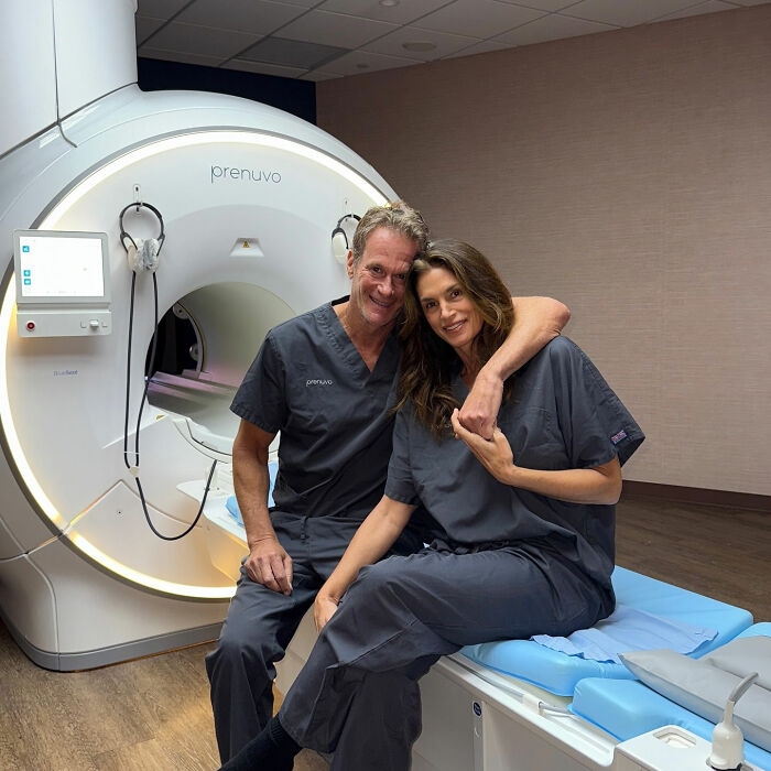 Cindy Crawford in scrubs sitting with a man by an MRI machine, highlighting full time job health routine debate. Cindy Crawford in scrubs sitting with a man by an MRI machine, highlighting full time job health routine debate.