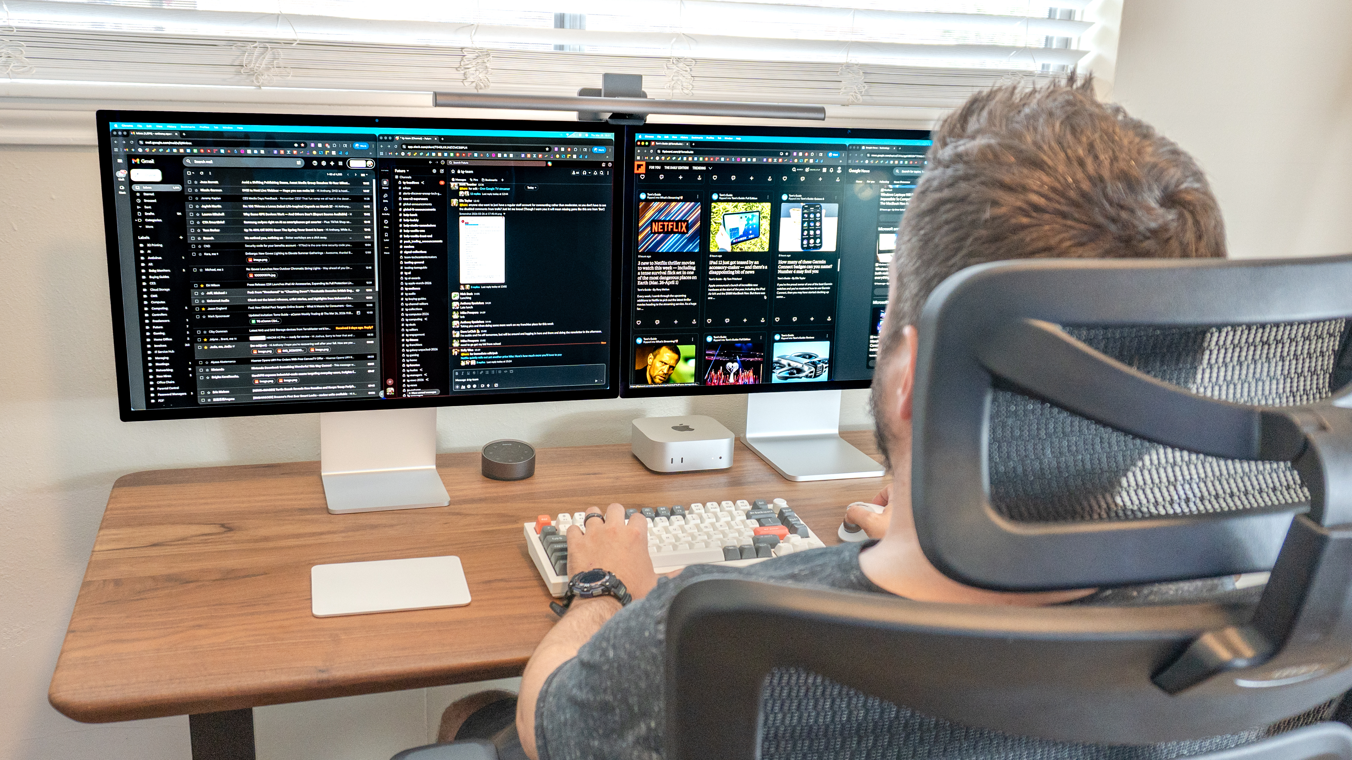 A person working at a desk setup with dual Apple Studio Display monitors side by side
