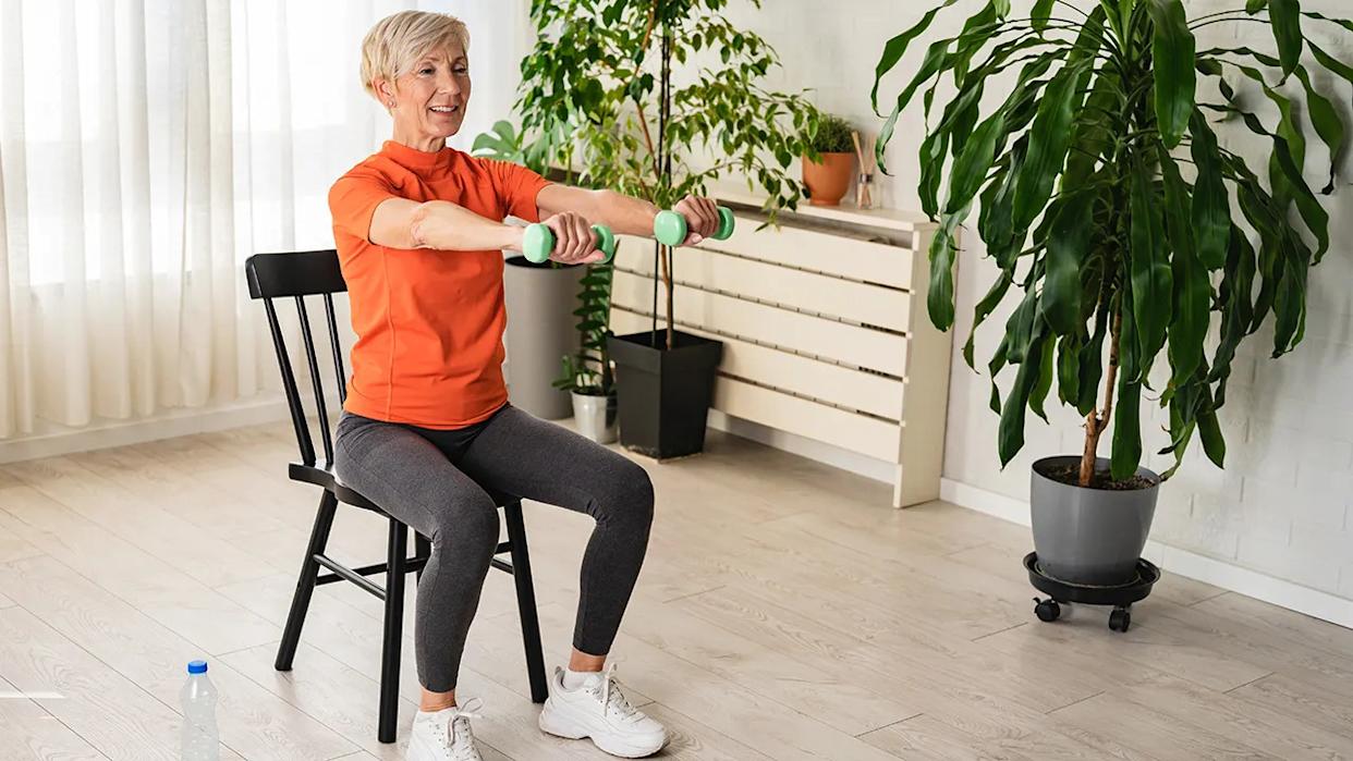 Smiling beautiful senior woman health instructor doing chair exercises with dumbbells