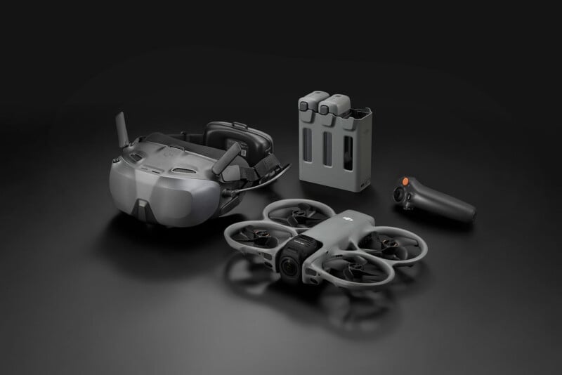 A set of gray drone accessories including an FPV drone, VR goggles, two batteries with a charging dock, and a hand controller, all displayed on a dark surface.