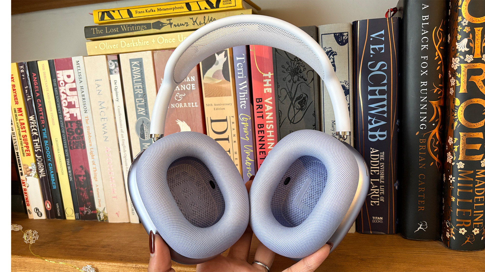 Apple AirPods Max 2 over-ear headphones held in hand in front of bookcase