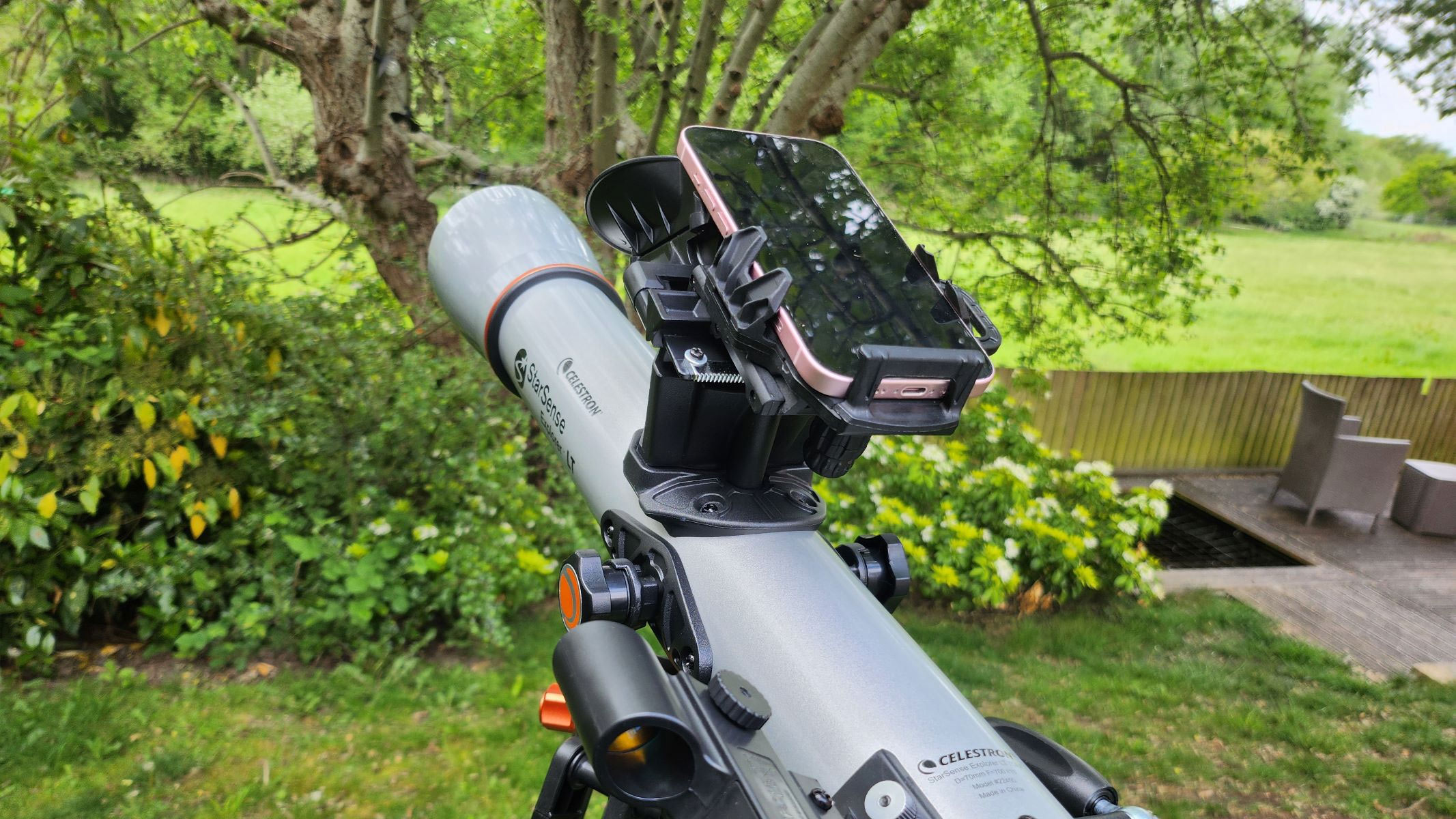 The Celestron StarSense Explorer LT 70AZ with a smartphone attached, in a garden.