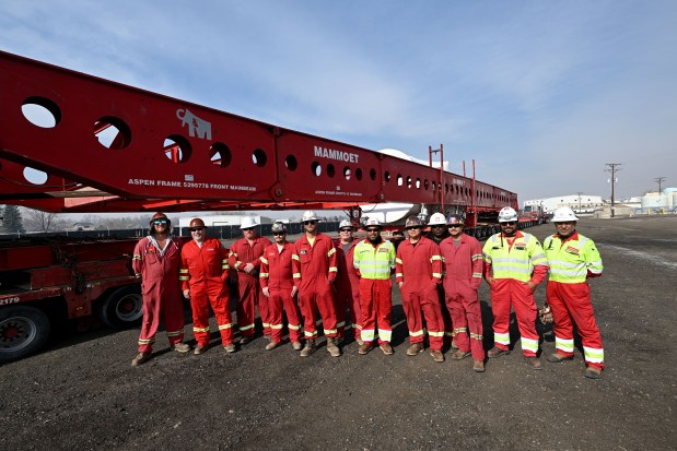 A crew from Mammoet takes a quick break to pose for a photo Friday, March 13, 2026, near some massive Xcel Energy equipment that weighs over 1 million pounds and is 300 feet long on a trailer in Loveland. The crew will move the turbine that is part of a natural gas operation bound for Xcel's Fort St. Vrain generating station near Platteville. (Jenny Sparks/Loveland Reporter-Herald)