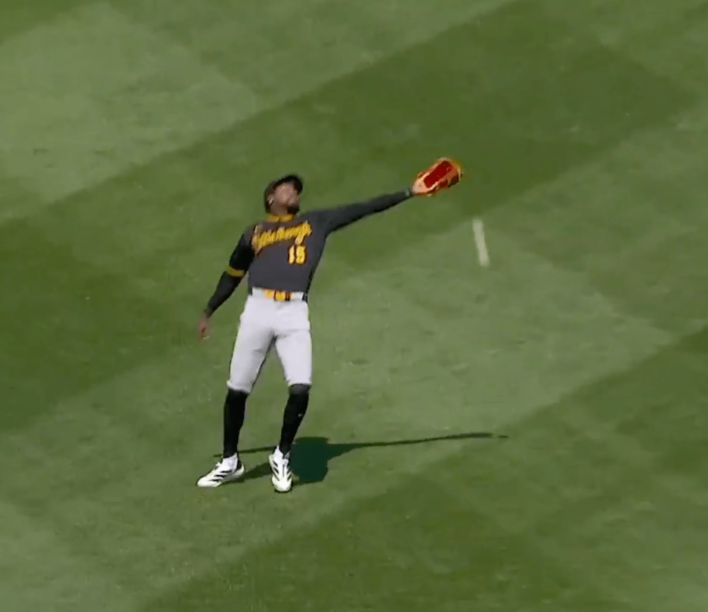 A baseball player in a gray and yellow uniform with number 15 reaching up with a red glove to catch a ball.