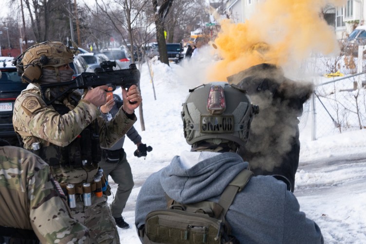 A yellow cloud exploded in the face of a man wearing a heavy coat as a uniformed federal agent fired at him from point-blank range in a snowy suburban environment.