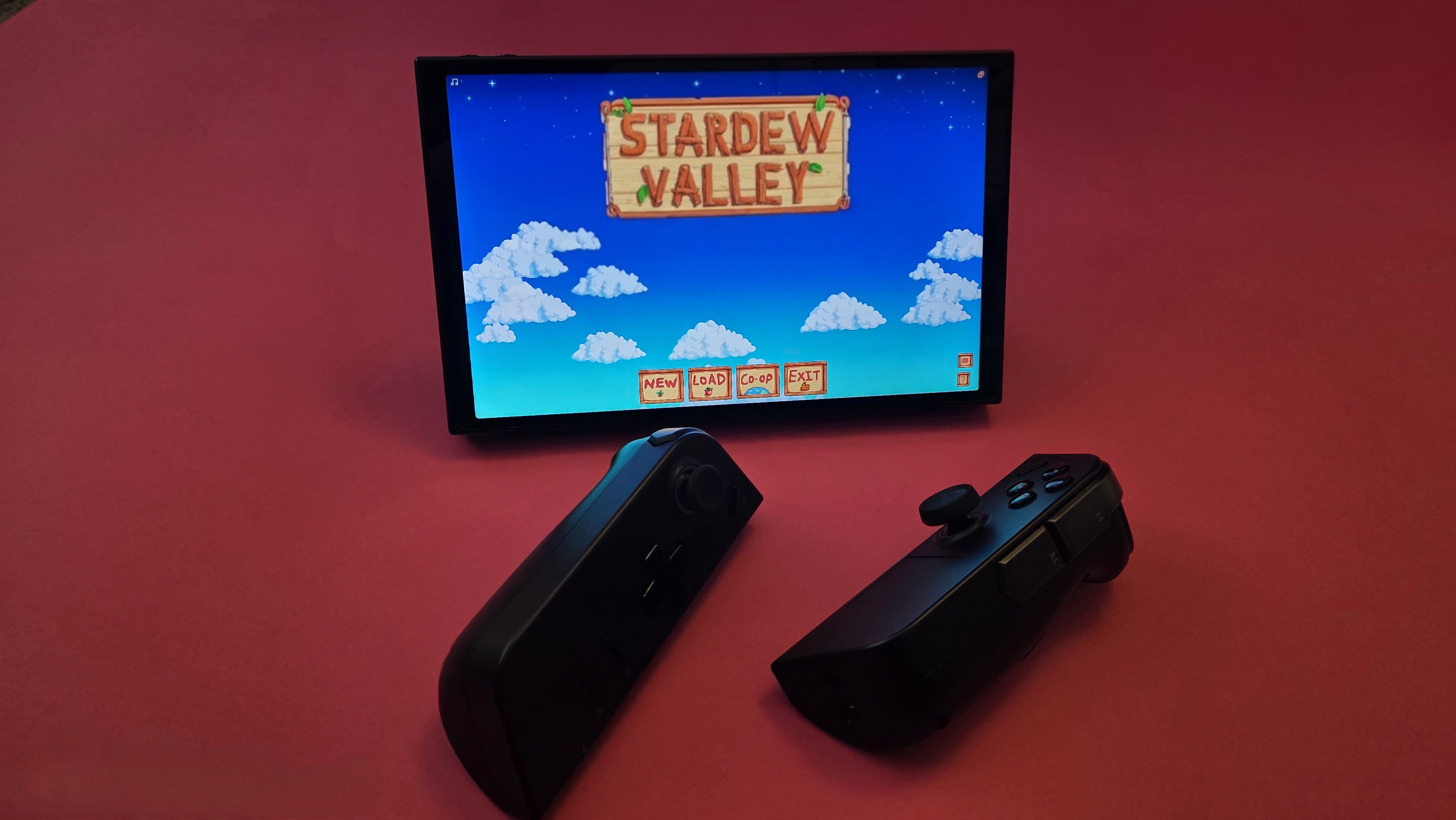 A handheld gaming device with a large screen and controls on each side rests on a pink surface.