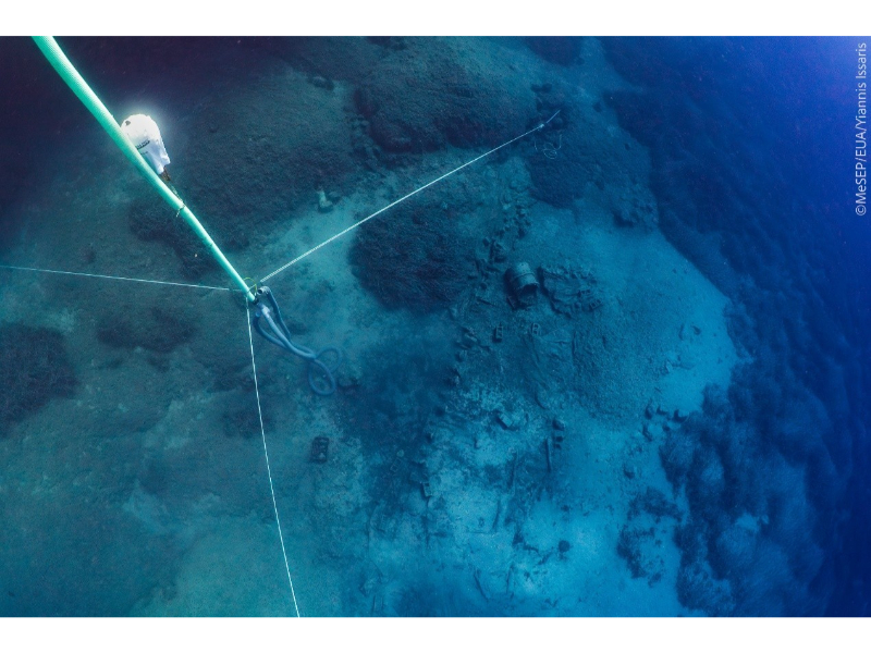 A view of a shipwreck on a sandy seafloor, the dark and light blue waters of the ocean mixing above