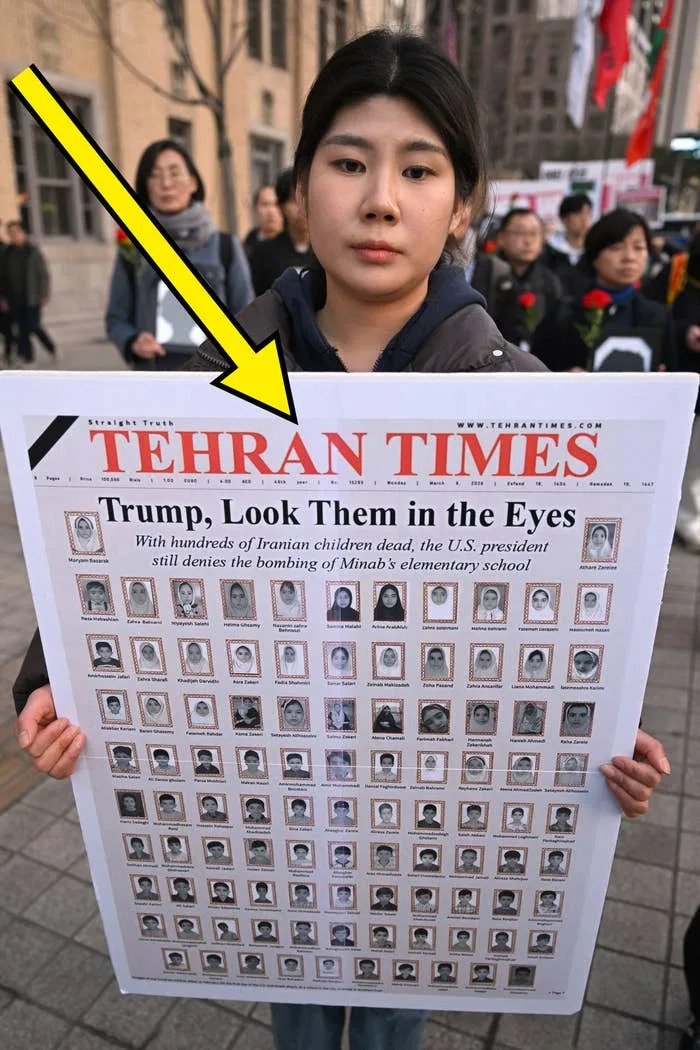 Person holding a poster resembling a Tehran Times front page, highlighting the impact of the bombing of Minab's elementary school