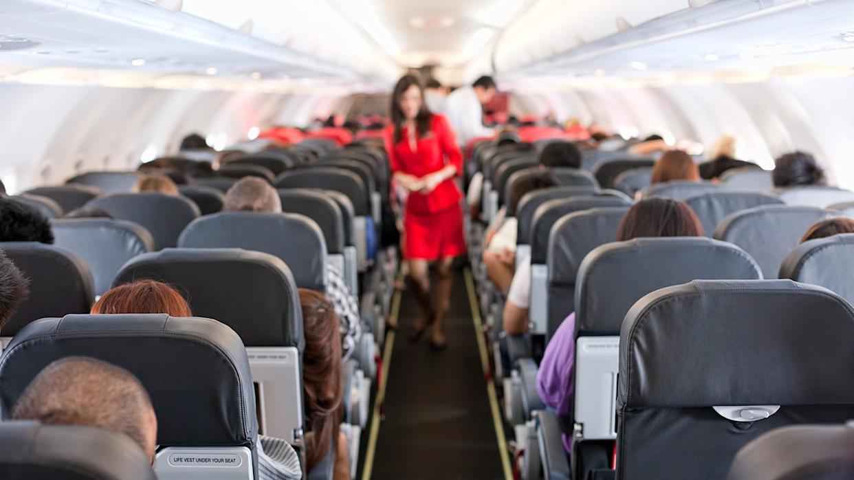A blurred flight attendant wearing red is seen standing in the cabin of a commercial flight.