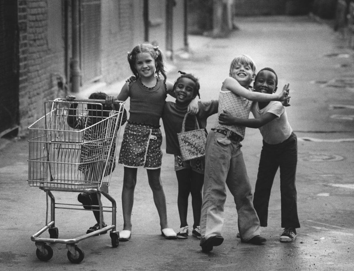A group of kids with their arms around each other, standing with a shopping trolley on a street in downtown Mount Clemens, Michigan -
