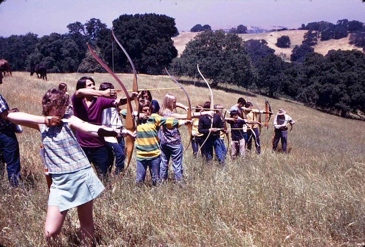 A line of about a dozen kids all aiming with their archery bows -